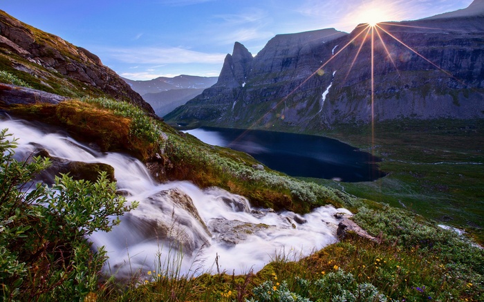 Waterfall flowing into a mountain lake with sunburst