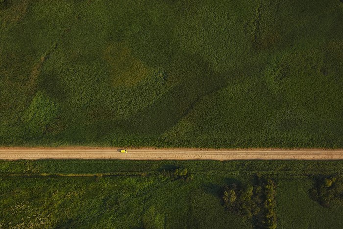 Yellow car on a dirt road through a green field