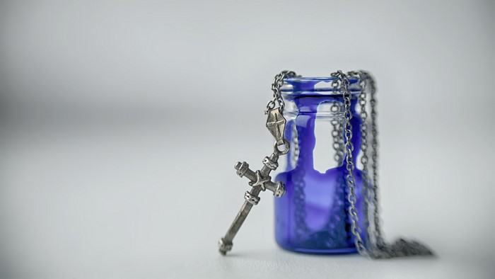 Silver cross necklace on a blue glass bottle