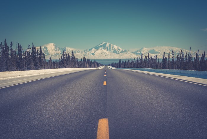 Empty road through snowy forest towards mountains in Alaska
