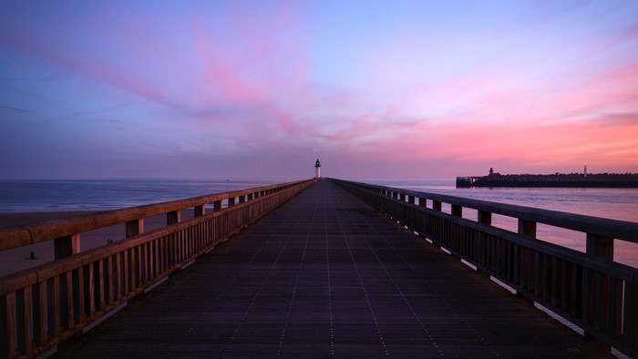 Pier with lighthouse at sunrise over the sea