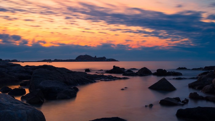 Sunset over the rocky Mediterranean coast with distant island