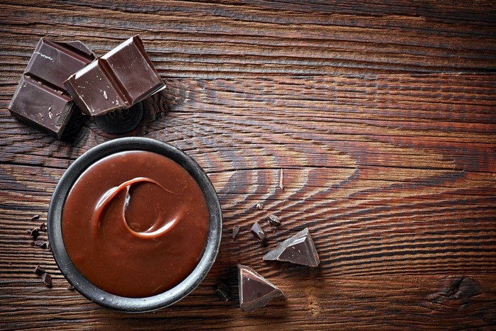Melted chocolate in a bowl with chocolate bars on a wooden surface