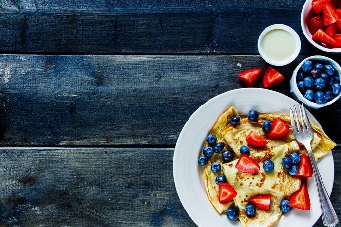 Pancakes with strawberries and blueberries on a dark wooden table