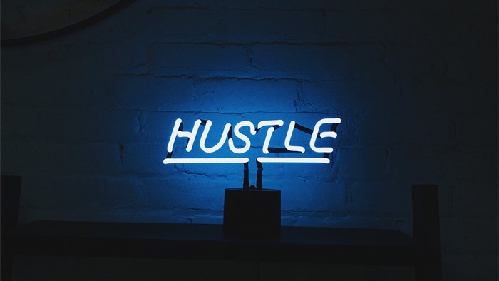 Blue neon sign that says HUSTLE on a brick wall