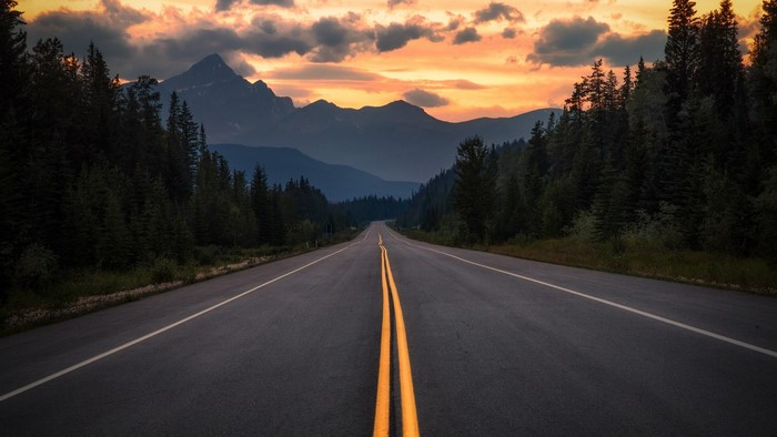 Road through mountains and forest at sunset