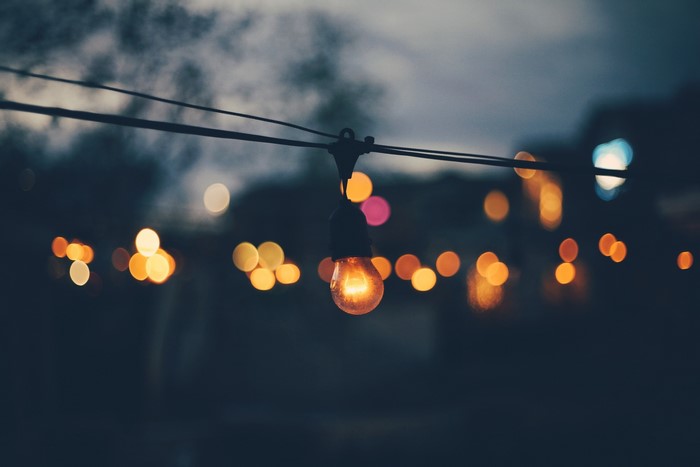 Single lightbulb on a string with bokeh lights at dusk