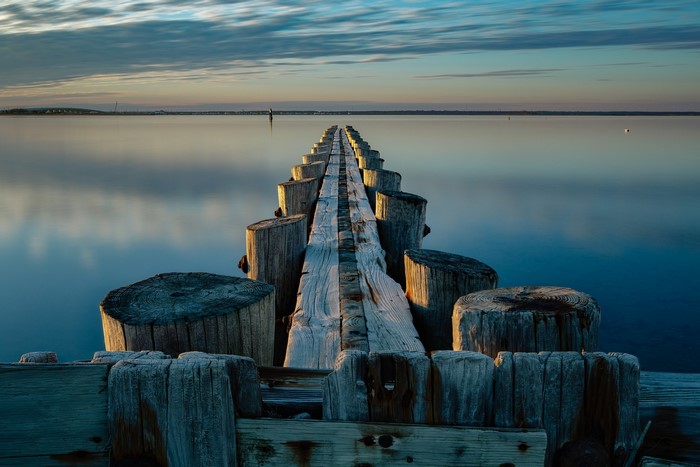 Wooden pier extending into calm water at sunset