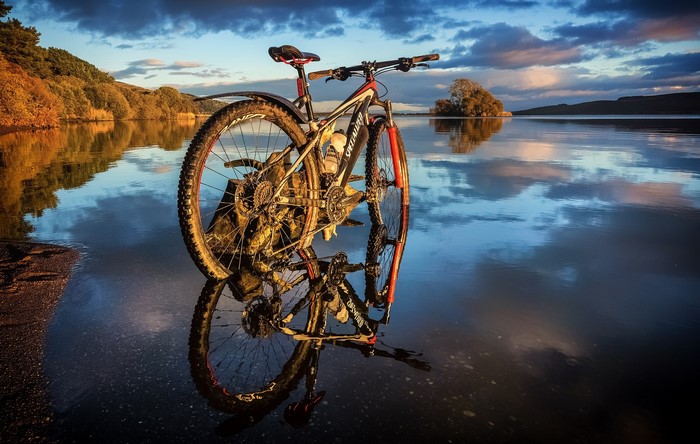 Mountain bike reflected in calm water at sunset