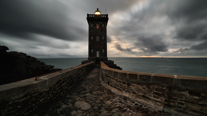 Lighthouse on a stone causeway under stormy sky