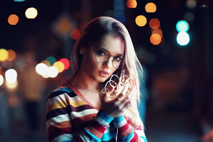 Woman with glasses holding fairy lights at night