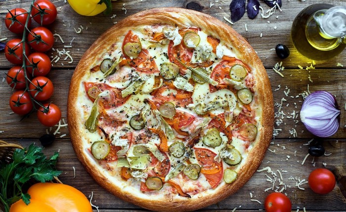 Pizza with tomatoes, cucumbers, and onions on a wooden table