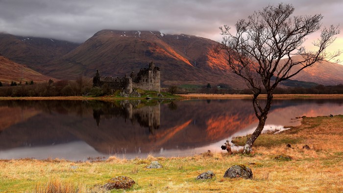 Castle ruin reflection on water with mountains and tree