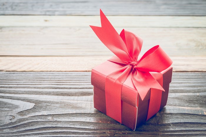 Red gift box with ribbon on wooden surface