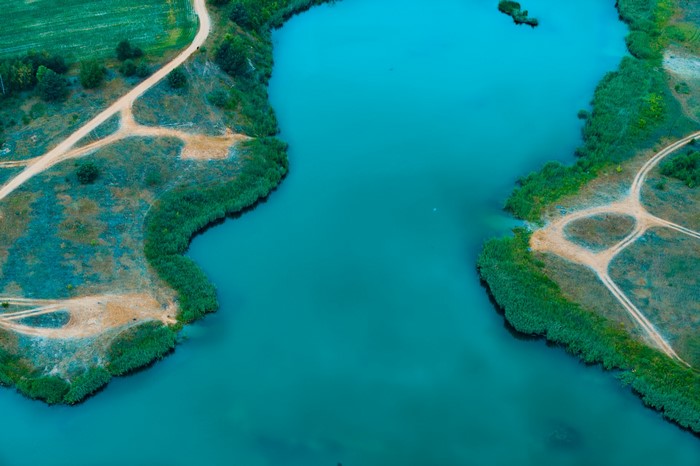 Aerial view of a turquoise lake with dirt roads and green shores