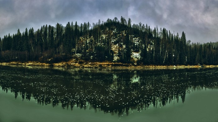 Panoramic view of a forest on a hill reflected in a lake