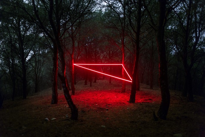 Red neon triangle in a dark forest