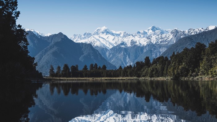 Snow-capped mountains reflected in a lake with trees