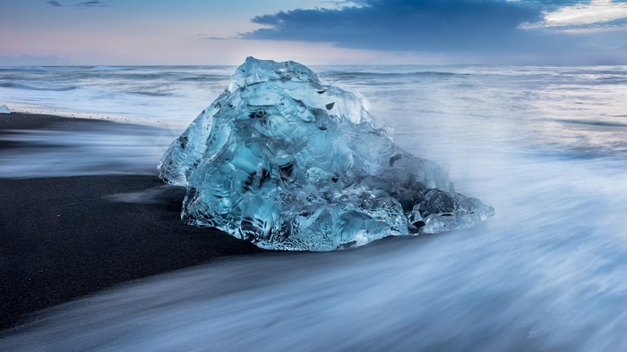 Iceberg on a black sand beach with ocean waves