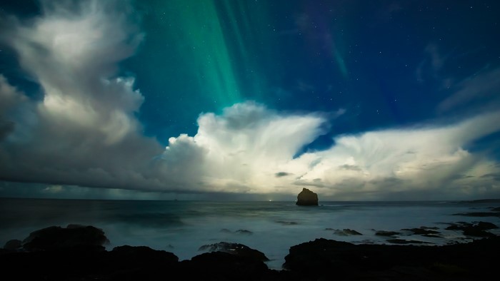 Aurora Borealis over the ocean with clouds and rocks