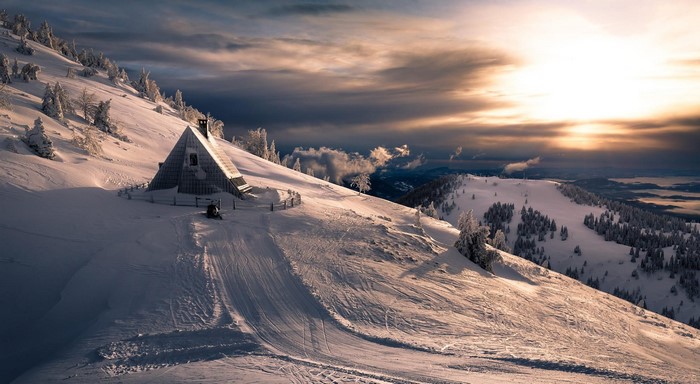 A-frame cabin on a snowy mountain at sunset