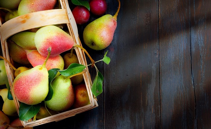 Pears and plums in a basket on a wooden table