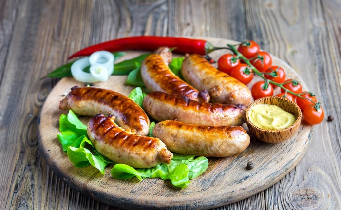 Grilled sausages with tomatoes and mustard on a wooden board