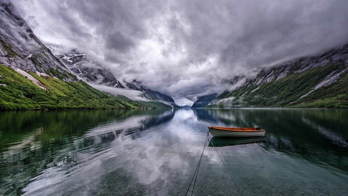 4K boat on a lake with mountains and clouds