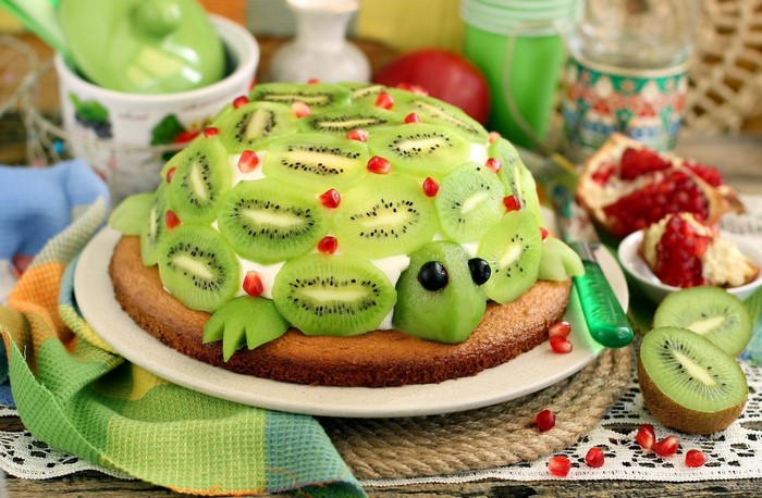 Turtle-shaped cake decorated with kiwi slices and pomegranate seeds