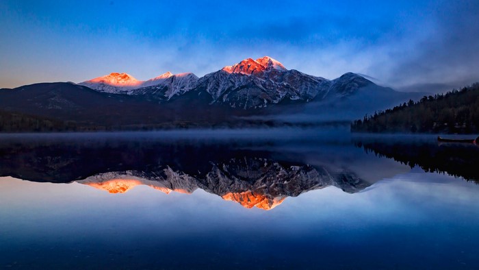 Sunrise over snowy mountains reflected in a misty lake