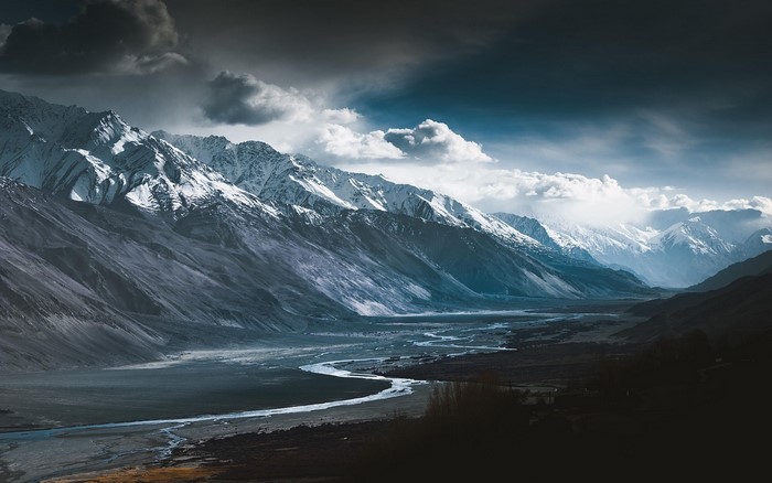 Snow-capped mountains and a winding river valley under a cloudy sky