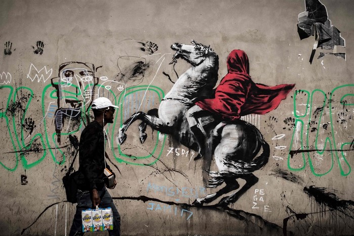 Man walks past graffiti of a person on a horse