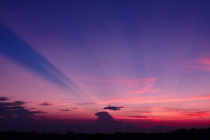 Purple sky with sun rays over landscape at sunset