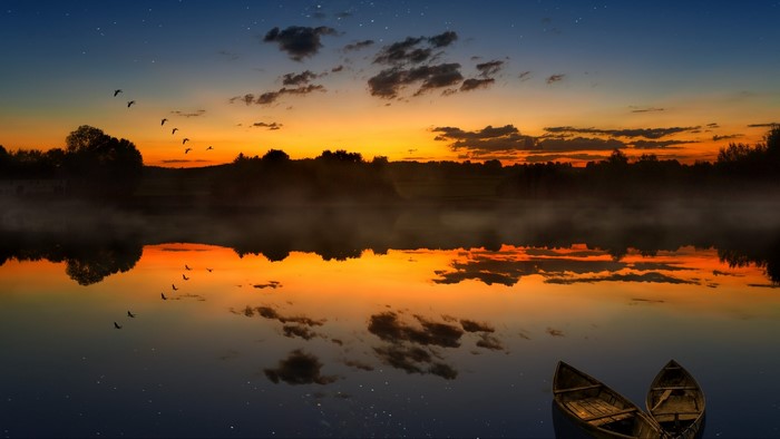 Sunset over a misty lake with birds and boats