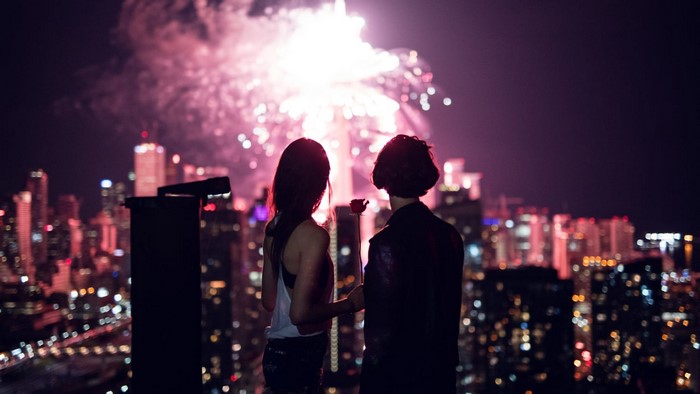 Two women watching fireworks over a cityscape at night