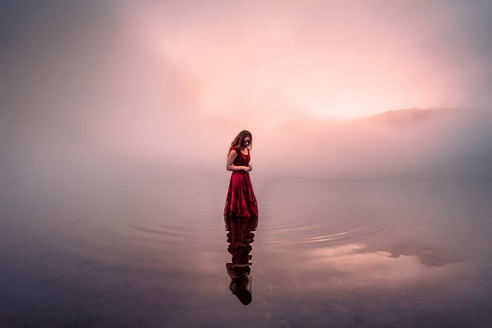 Woman in red dress standing in misty water with reflection