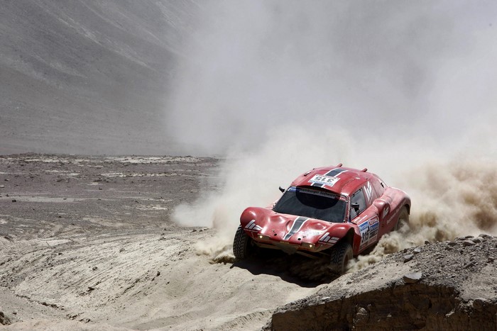 Red rally car racing through a dusty desert landscape