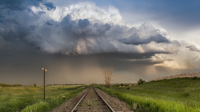 Train tracks leading towards a stormy sky