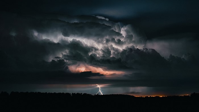 Lightning strikes through dark storm clouds over a silhouetted landscape