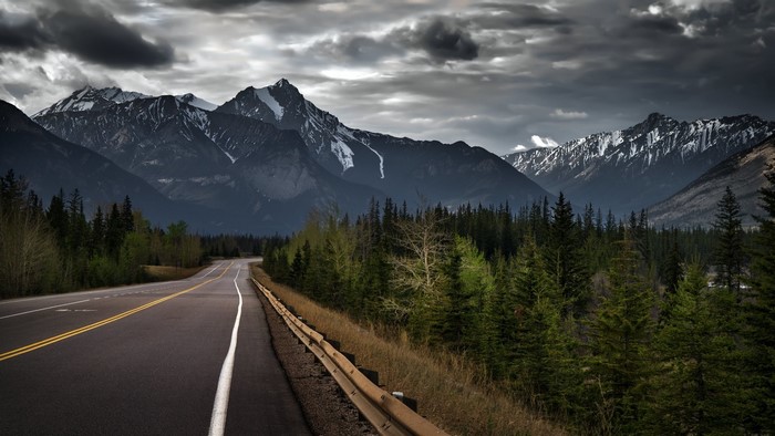 Road leading to snow-capped mountains under overcast sky
