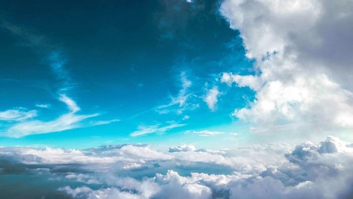 Cyan sky with white clouds above a sea of clouds
