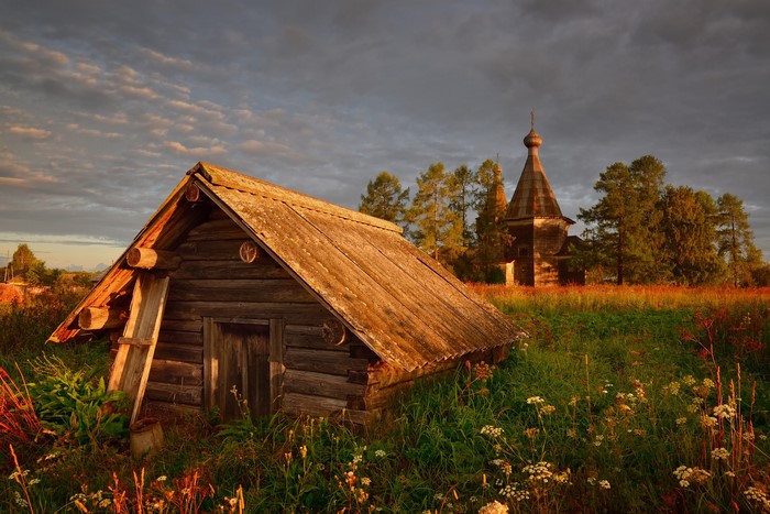 Wooden cabin and church in a field at sunset