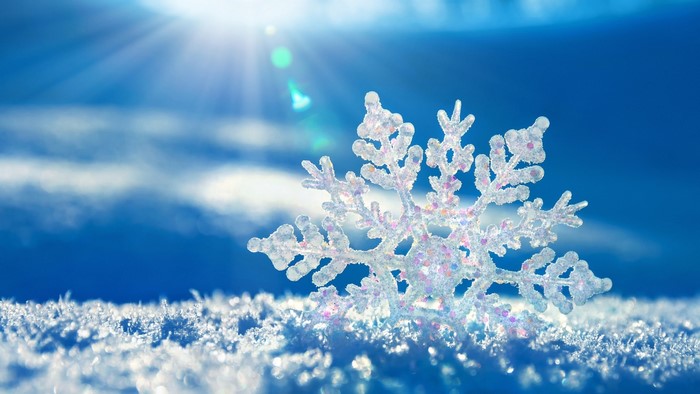 Close-up of a sparkling snowflake on snow with sun rays