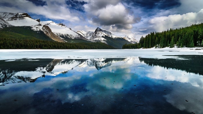Frozen lake reflecting snow-capped mountains and forest in Canada