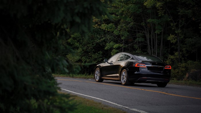 Black Tesla Model S driving on a road through trees