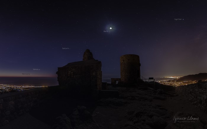 Planets visible in the night sky over ruins and a city