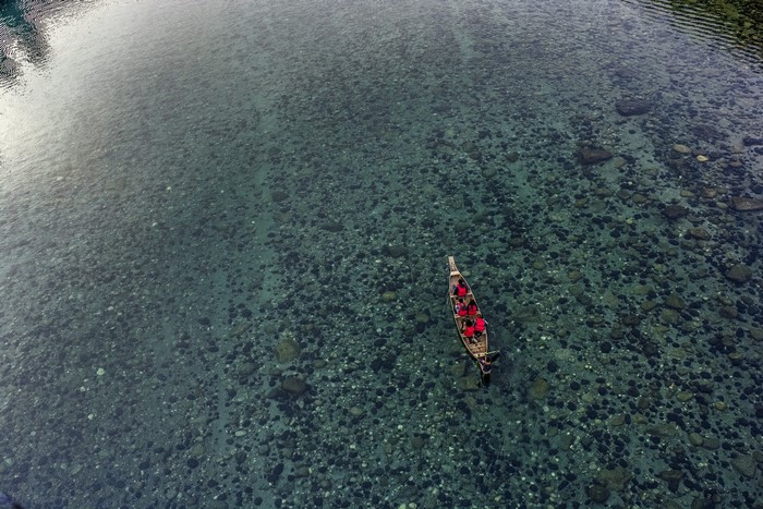 People in a boat on a clear river with rocks