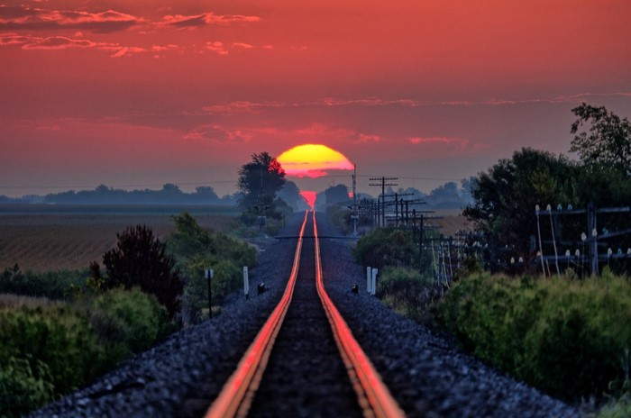 Railway tracks at sunset with sun and clouds