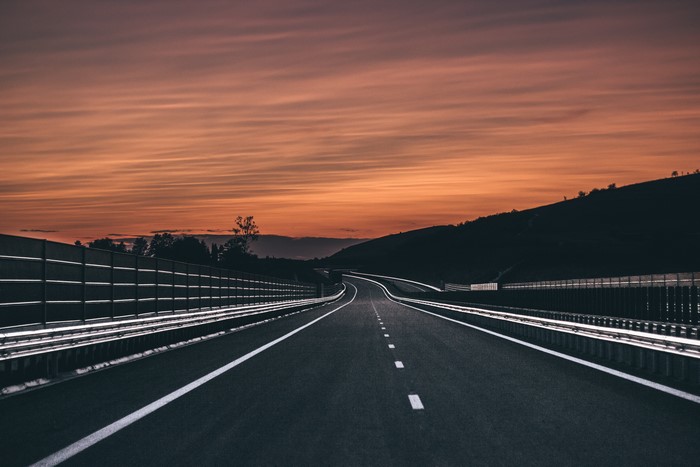 Empty highway at sunset with a hill and fence