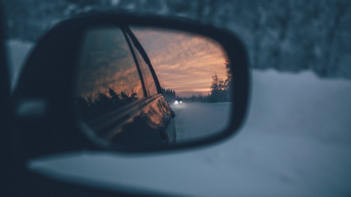 Rearview mirror reflection of a snowy road at sunset